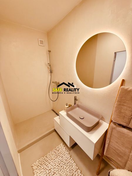A bathroom in a 3-room apartment with a large illuminated mirror and a shower without a door.