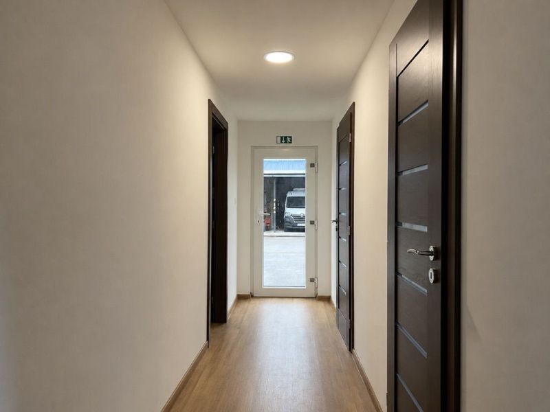 A corridor with a wooden decor floor and dark doors in manufacturing premises.