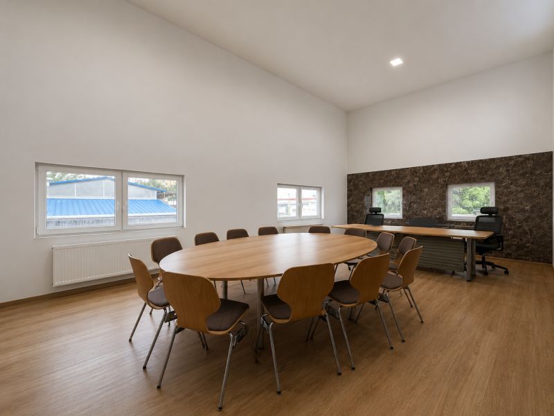 Conference room with a large table, chairs, and office desks, floor with wooden decor.