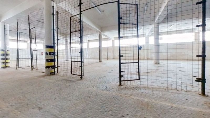 A fenced interior of a warehouse and hall with open gates and bright walls.