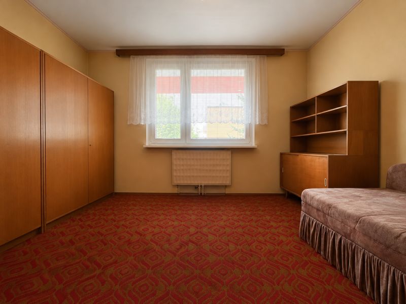 Living room in a two-room apartment with a red carpet, old furniture, and a window.