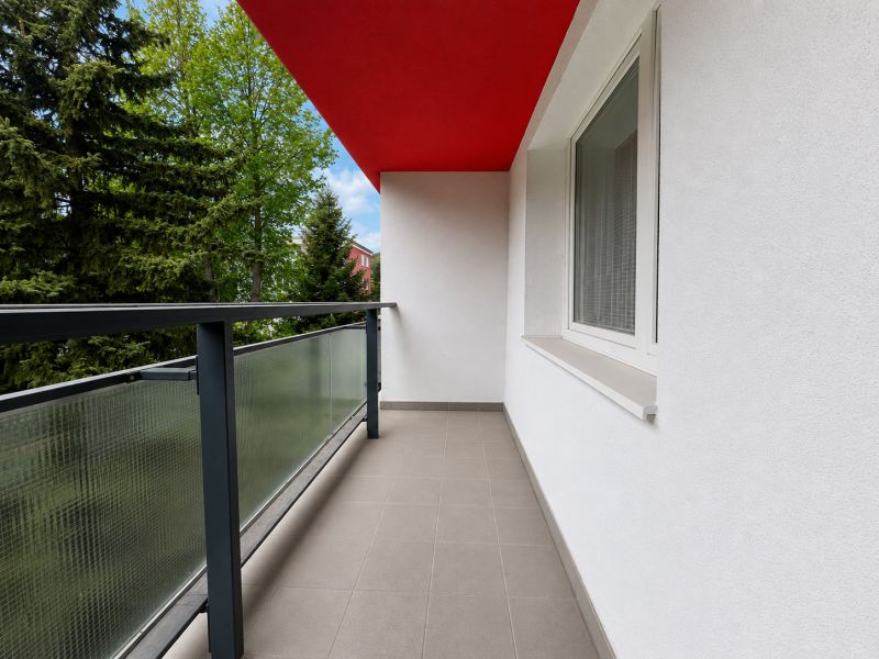 Balcony from a 2-room apartment with a red ceiling and railing with glass.