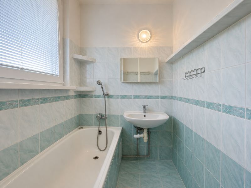 Bathroom with a bathtub and a sink, blue tiles in a 2-room apartment.