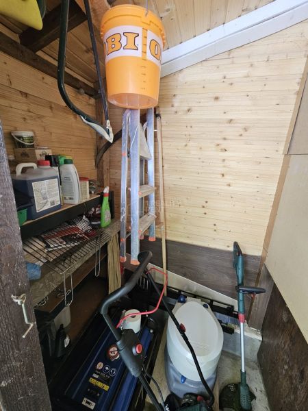 There is a shed in the garden with tools and shelves for storage.