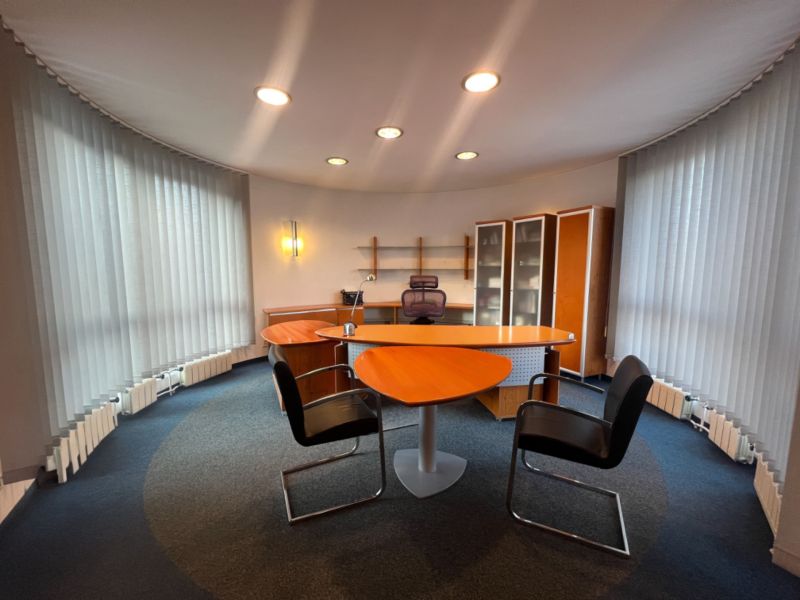 An office with a wooden decor desk, shelves, and illuminated vertical blinds.