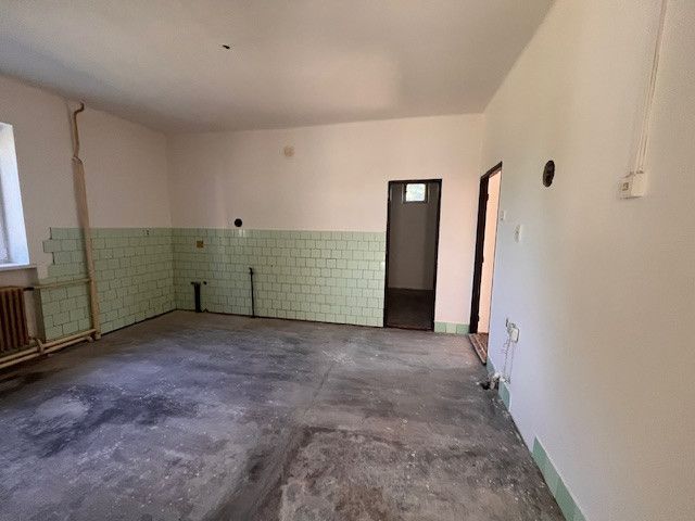 A room in a family house with an unfinished floor and green tiles.