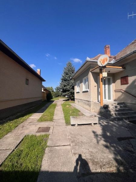 The exterior of a family house in Vrakúň, a sidewalk, a lawn, a tree, and a blue sky.