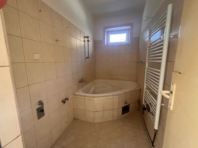 A bathroom in a family house with a corner bathtub and a radiator on the wall.