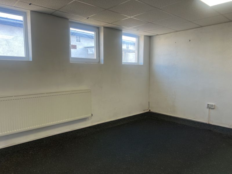 A room with windows, a radiator, and a rubber floor in a warehouse and halls.