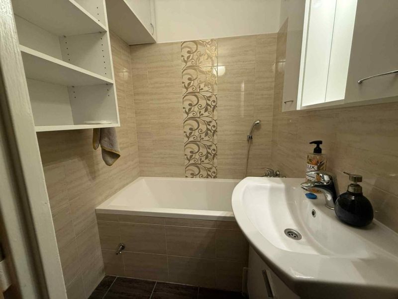 A bathroom with a bathtub in a 4-room apartment, with storage shelves and decorative tiles.