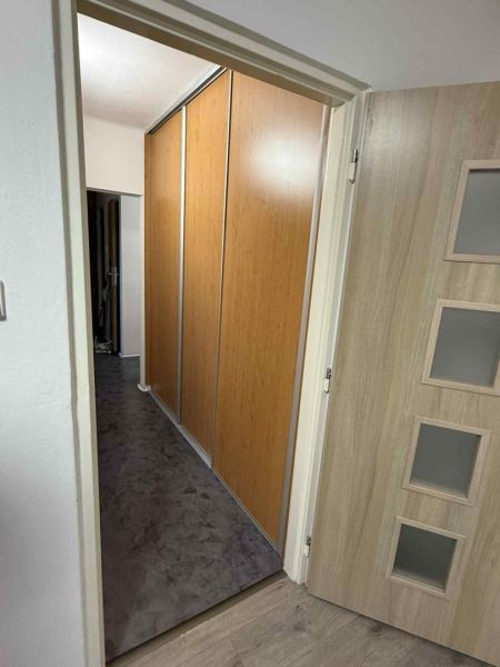 An open door in a 4-room apartment with a wood-patterned floor and a built-in wardrobe.