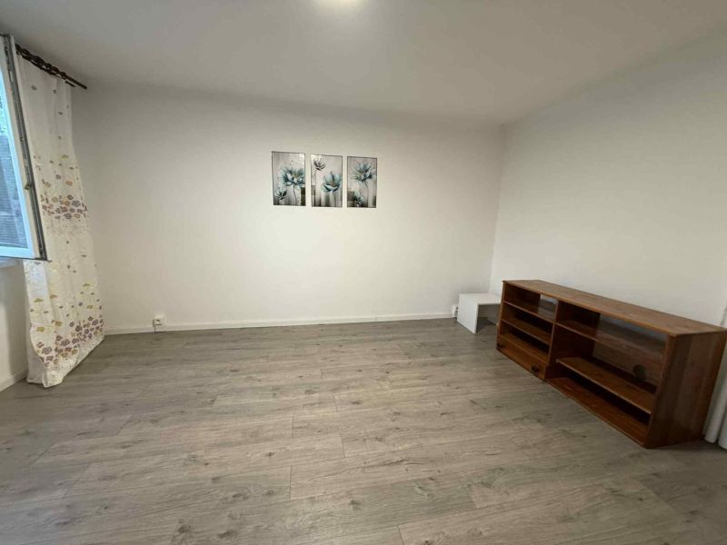 Living room in a 4-room apartment with a wooden decor floor, a shelf, and paintings on the wall.