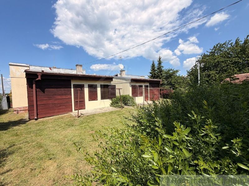 A cottage in Nové Zámky surrounded by lawn and bushes under a blue sky.
