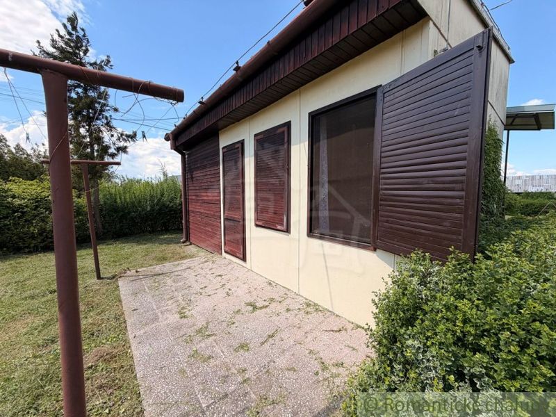 A cottage in Nové Zámky with closed wooden shutters and surrounding greenery in the garden.
