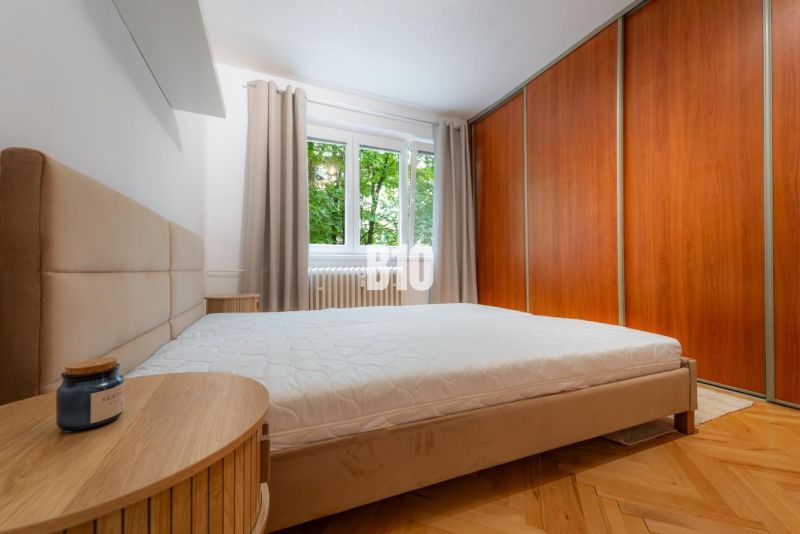 A bedroom in a two-room apartment with a wooden decor floor and a built-in wardrobe.