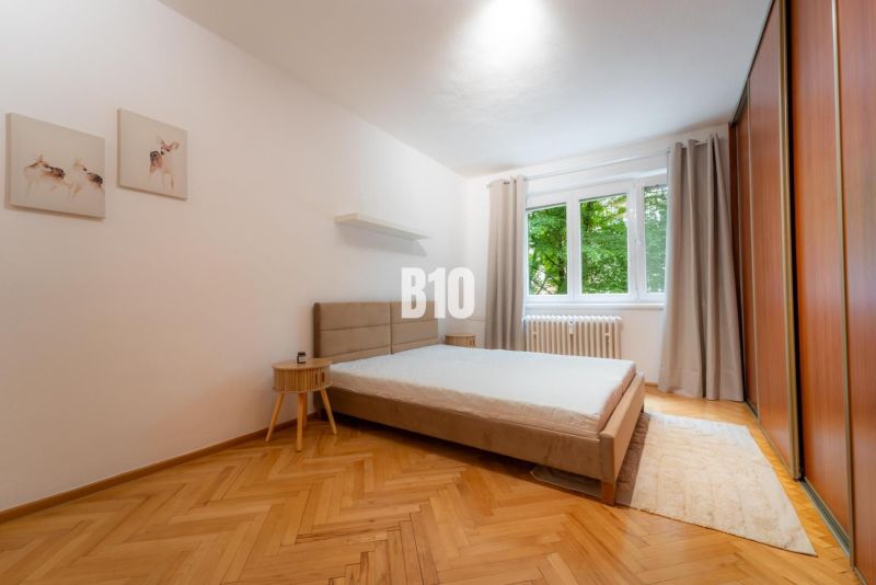 Bedroom in a two-room apartment with a large bed, wooden decor flooring, and a wardrobe.