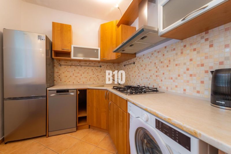 A kitchen with a tiled wall, appliances, and a wooden decor floor in a two-room apartment.
