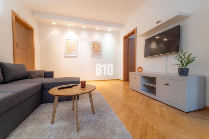 Living room with a TV on the wall, a gray sofa, and a floor with a wood decor.