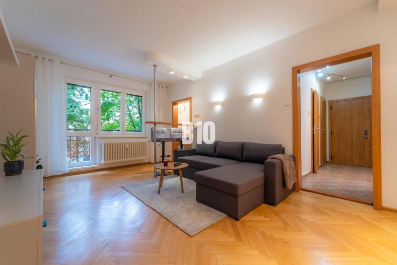 Living room in a two-room apartment with a wooden decor floor and a large window.