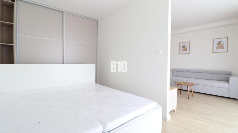 Bedroom with a wardrobe, bed, sofa, and wooden decor flooring in a 2-room apartment.