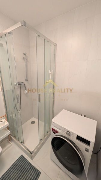 A bathroom with a glass shower enclosure and a washing machine in a 2-room apartment.
