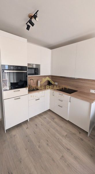 A kitchen in a 2-room apartment with built-in appliances and a wooden decor floor.