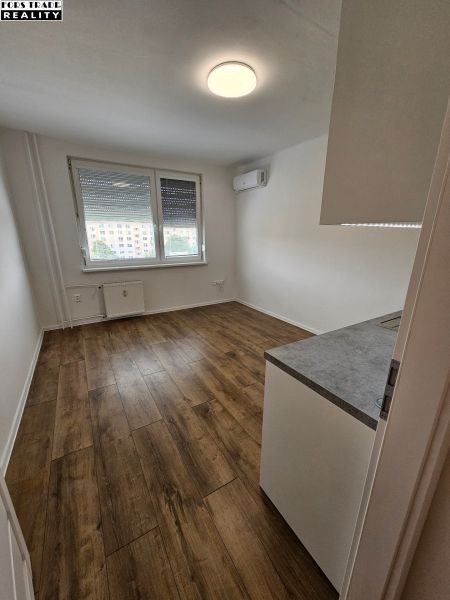 A studio apartment with a wooden decor floor, air conditioning, and a large window for light.