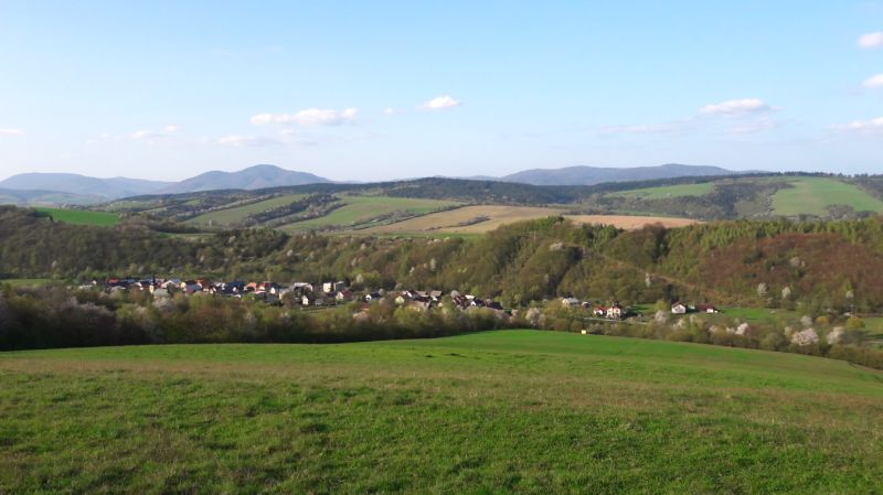 A view of agricultural and forest lands in Bogliarka with a hilly horizon and a village.