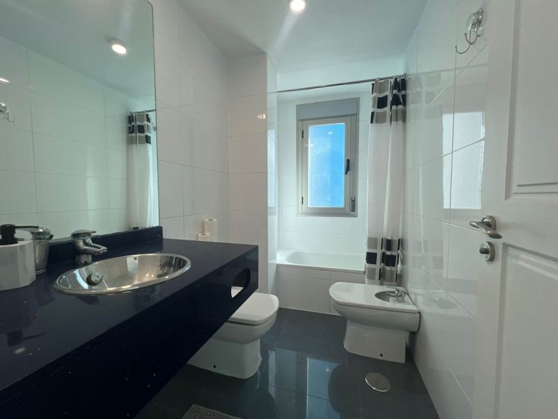A bathroom in a holiday apartment with a bathtub and a sink on a dark countertop.