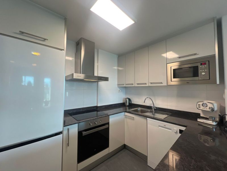 A kitchen in a holiday apartment with white cabinets, appliances, and a black countertop.