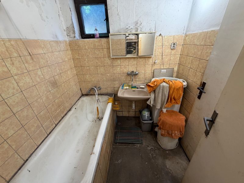 A bathroom in a family house with a bathtub, sink, and beige tiles on the walls.