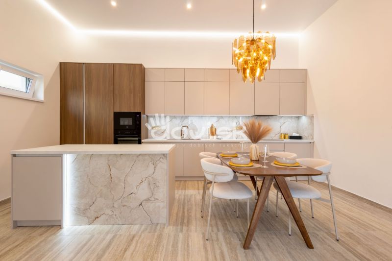 A kitchen with an island, a wooden decor floor, a dining table, and a golden chandelier.