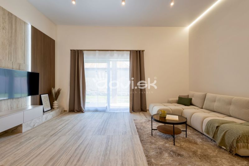 Living room of a family house with a sofa, wood-patterned floor, and a TV on the wall.