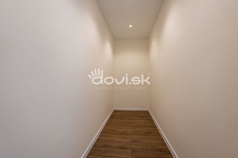 A narrow hallway in a family house with white walls and a wooden-patterned floor.