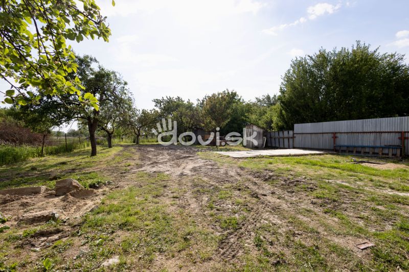 A plot of land in Zemplínska Široká with grass, trees, and a metal fence near a family house.