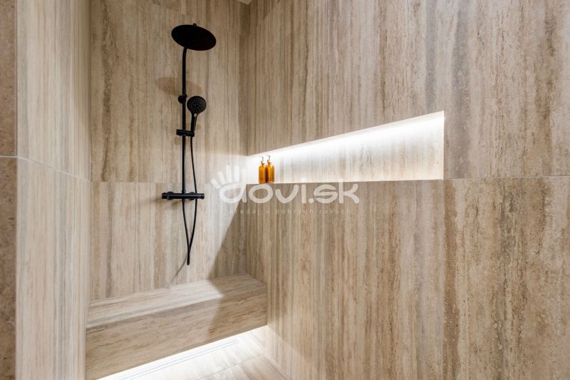 Shower enclosure with natural stone tiles and black fittings in a family house.