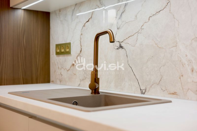 Kitchen faucet and countertop in a family house with a marble wall decor.