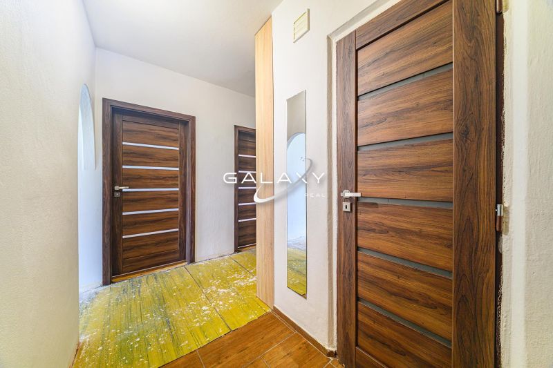 A hallway in a 3-room apartment with wooden doors and a floor with a wooden decor.
