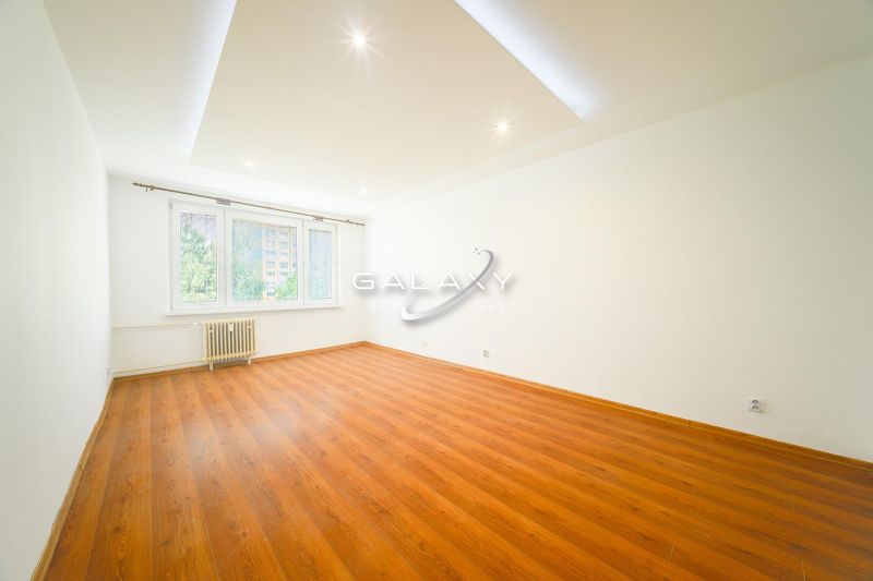 Spacious living room with wood-patterned flooring in a 3-room apartment, white walls.