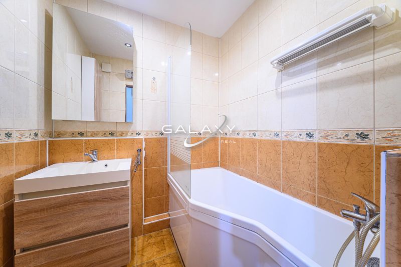 A bathroom with a bathtub and a sink in a 3-room apartment with tiles and a mirror.