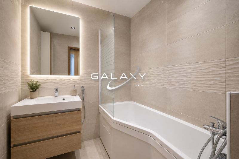 A bathroom in a 3-room apartment with a bathtub, a sink, and a floor with a wooden decor.
