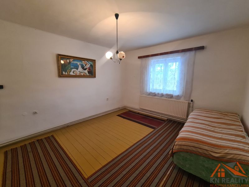 Interior of a family house with a bed, a painting, and a window with curtains.