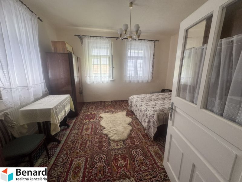 A room in a family house with a carpet, bed, table, and curtains on the windows.