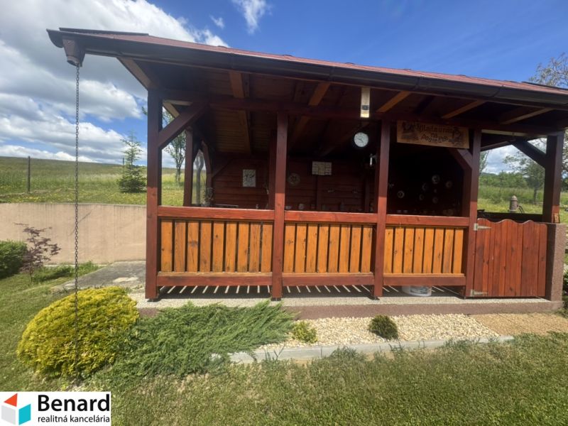 A wooden gazebo by a family house in Orlov, surrounded by a landscaped garden and a hedge.