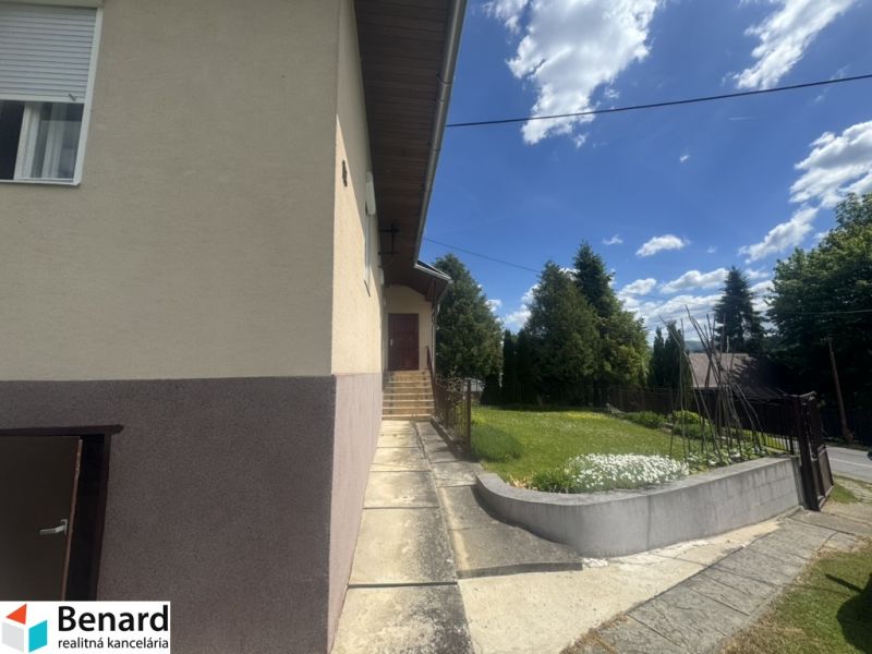 A family house in Orlov with a walkway and greenery, surrounded by trees and a blue sky.