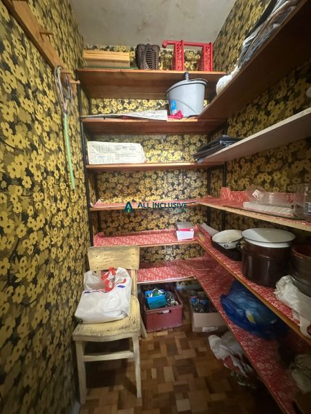 A pantry in a 2-room apartment with floral wallpaper and storage shelves.