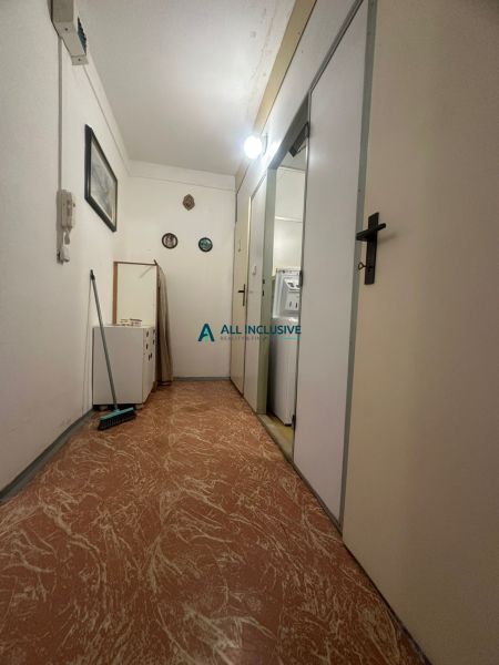 A hallway in a 2-room apartment with a wooden decor floor, white walls, and light.