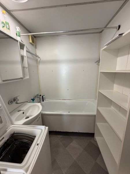 A bathroom in a 3-room apartment with a bathtub, sink, washing machine, and shelving cabinet.