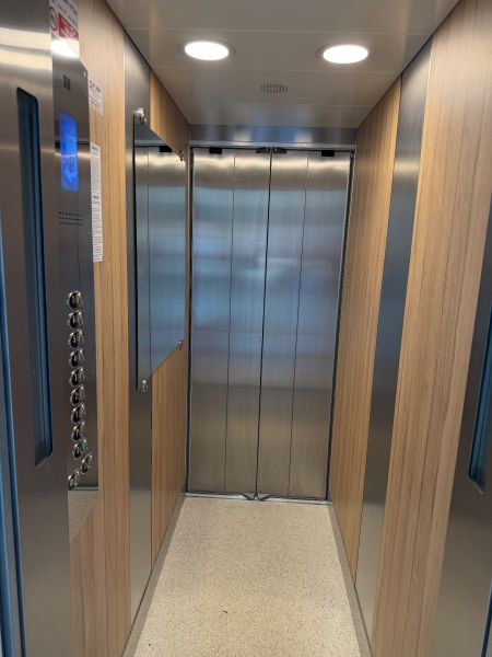 An elevator with a wooden decor floor and metal walls.
