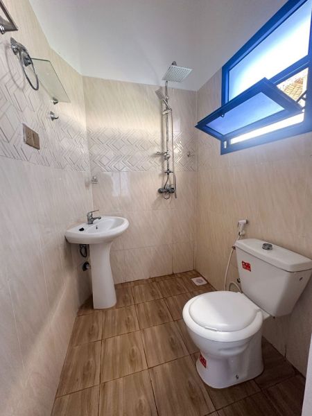 Bathroom with a sink, shower, and toilet in a family house, floor with wood decor.